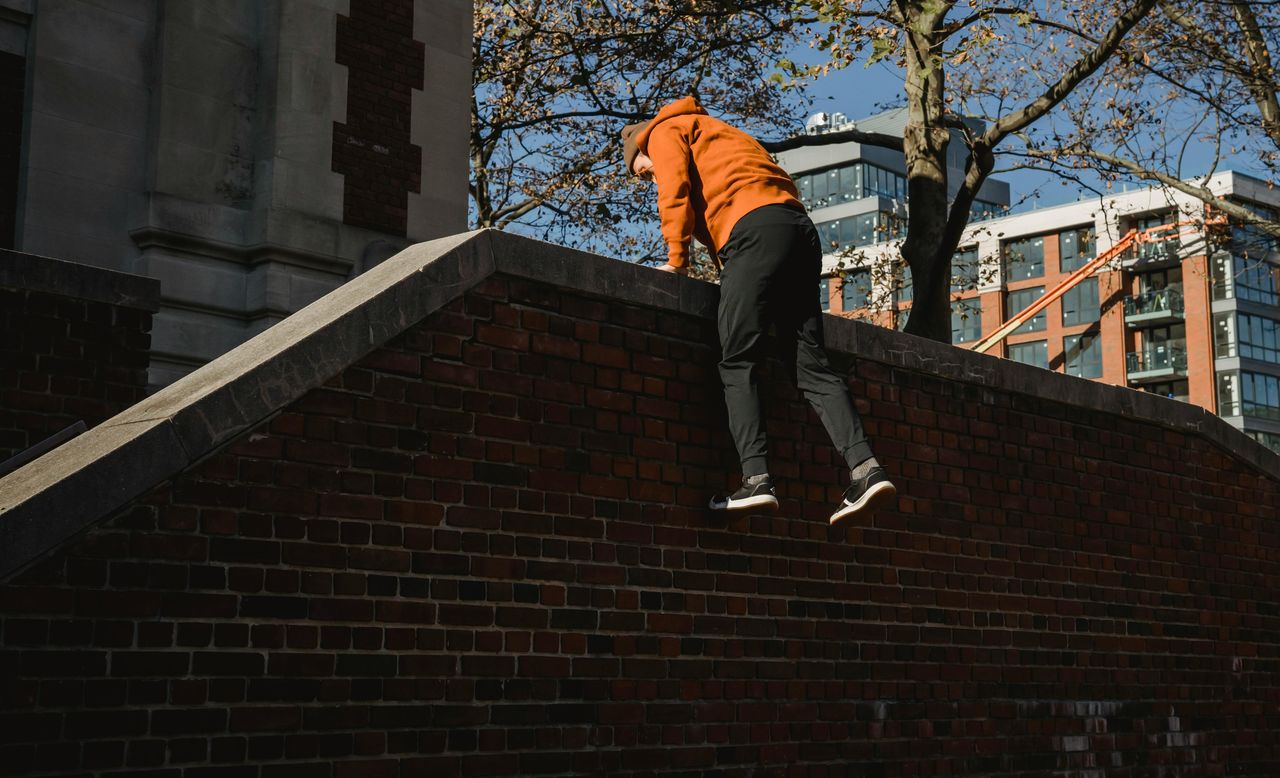 sporty tracer climbing on brick fence in autumn town