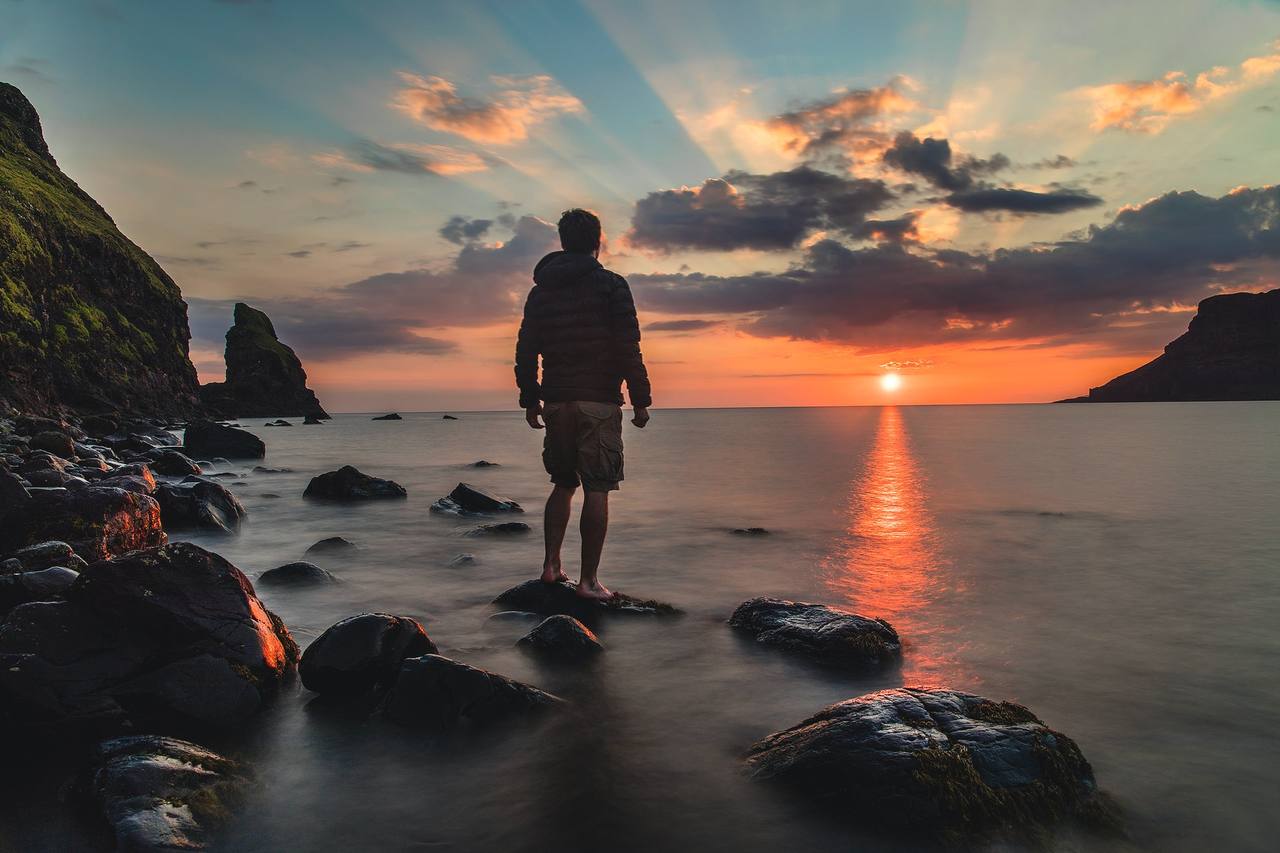 A person standing on rocks at the shoreline watching a brilliant sunrise over the sea