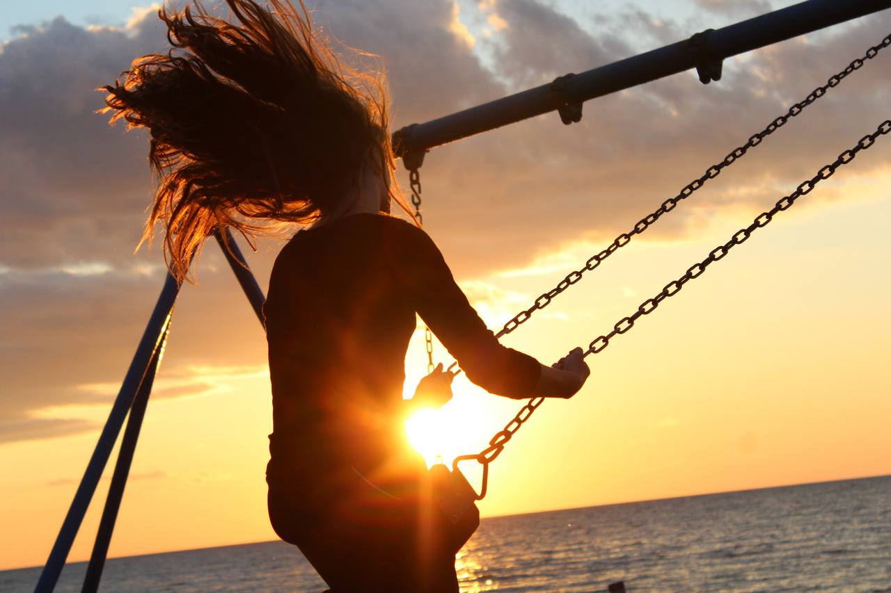 A person on a swing at sunset with hair caught in the wind